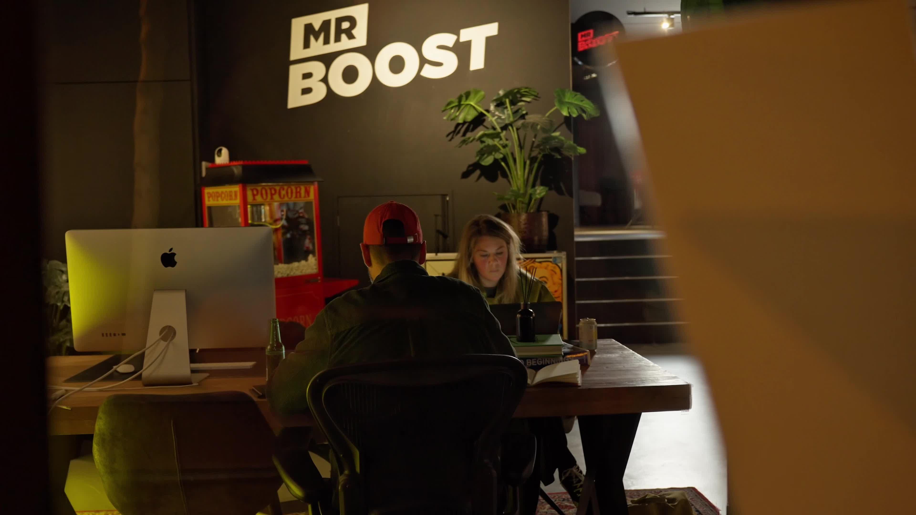 MRBoost team members collaborating at a studio table beneath the MR BOOST wall logo