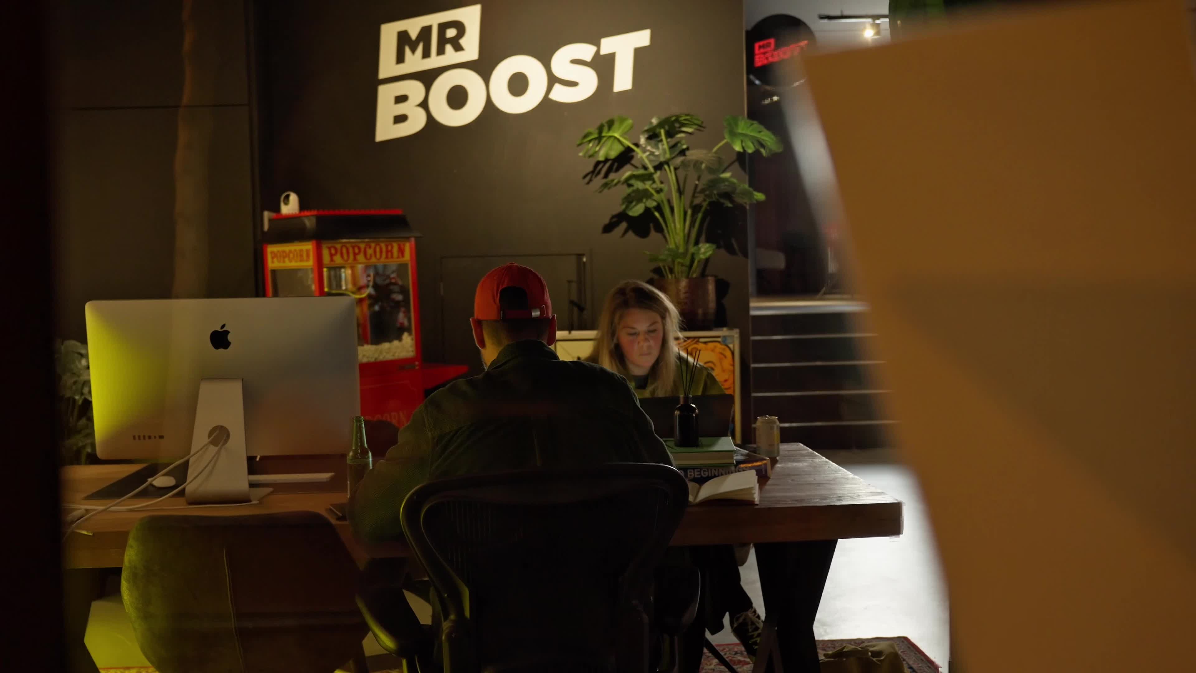 MRBoost team members collaborating at a studio table beneath the MR BOOST wall logo